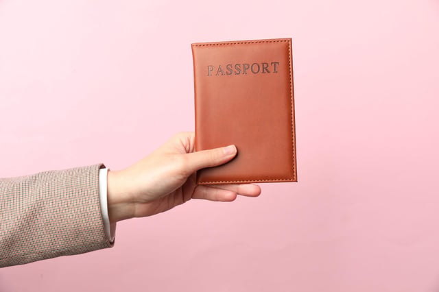 Woman Holding Passport in Bright Cover on Pink Background